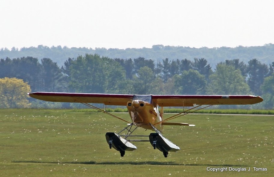 A Piper Super Cub on amphibious floats lands in the grass at Brodhead Airport.